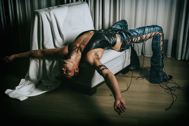 Model draped backwards over a white lounge chair wearing laced denim pants and black top