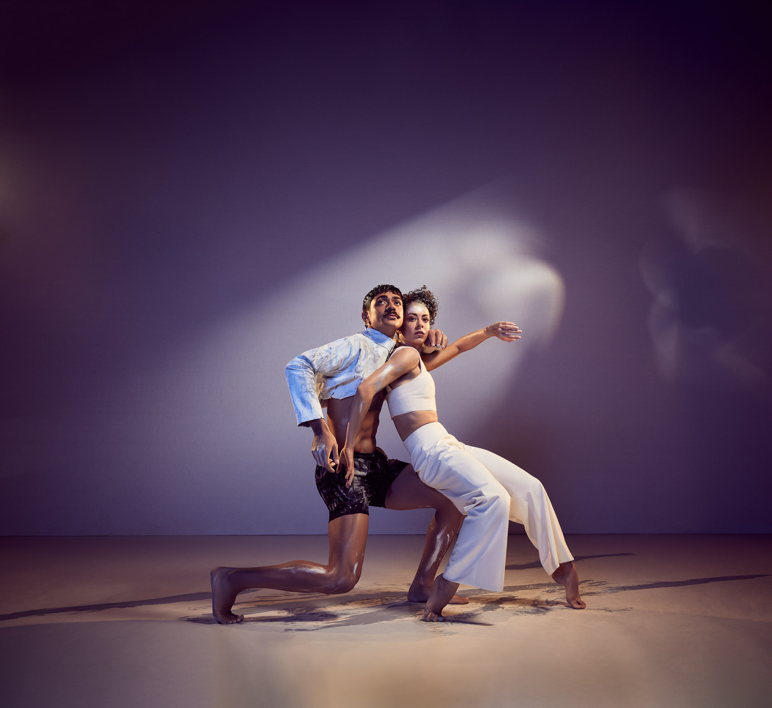 Two dancers posing together under dramatic spotlight against a dark grey studio background by photographer Daniel Boud.