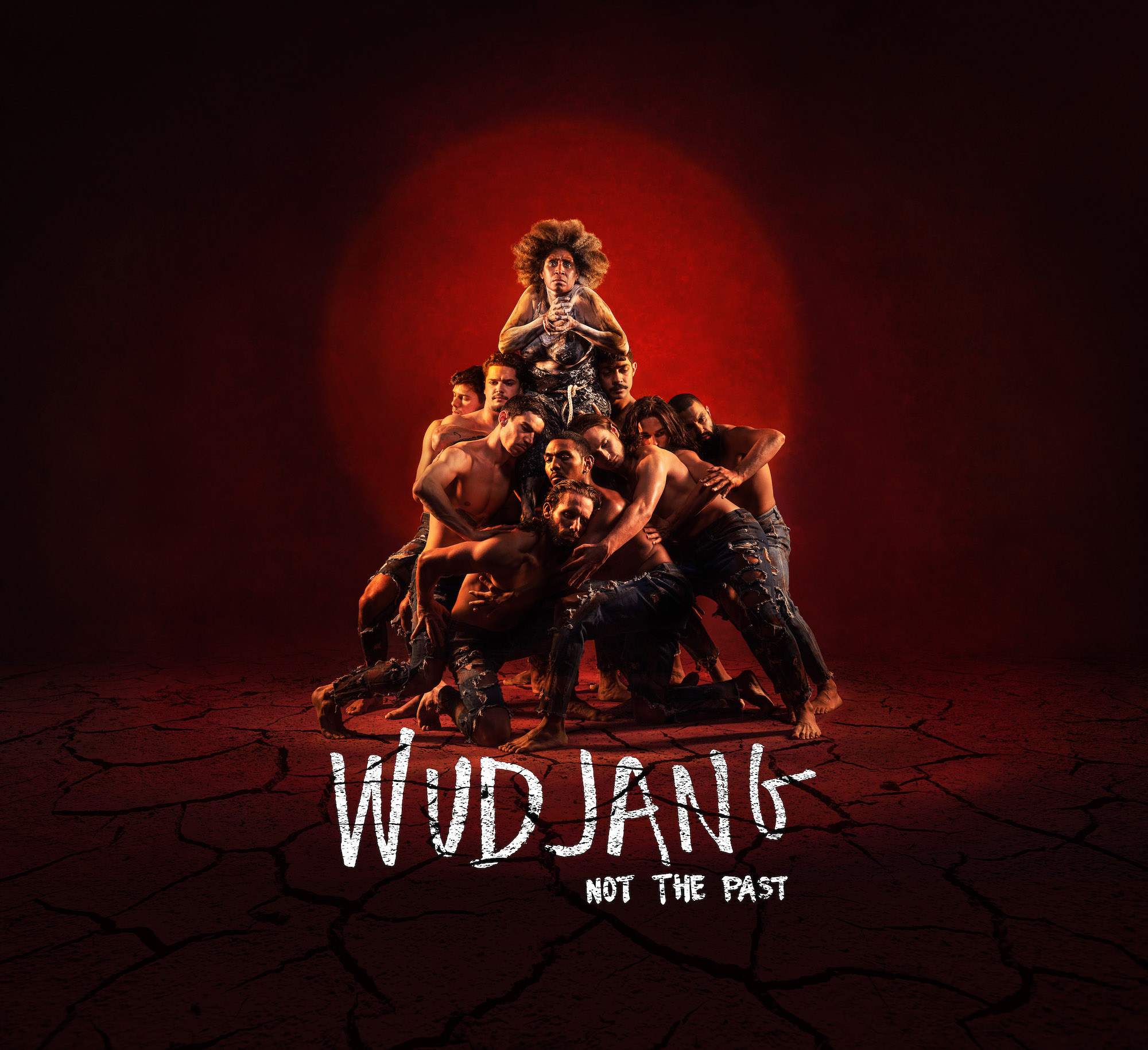 Group performance art features a diverse ensemble of shirtless men supporting a singer in a red-lit studio, creating a dynamic visual.