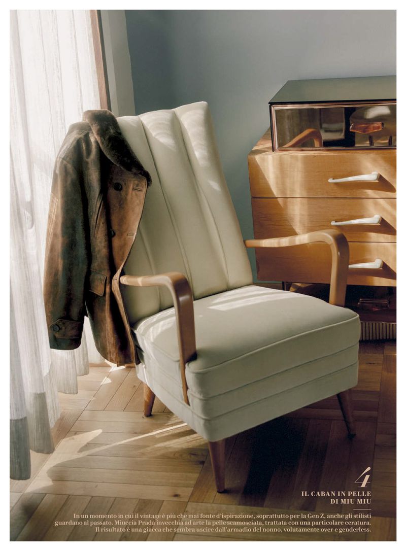 Beige chair with wooden frame in a room with brown coat hanging on it, next to wooden drawers under natural window light.