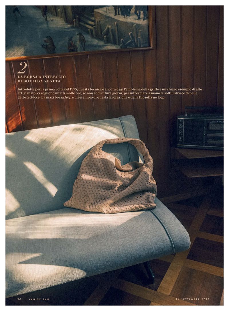 Woven Bottega Veneta handbag resting on a grey upholstered sofa in a room with wood paneling and a framed painting in the background.