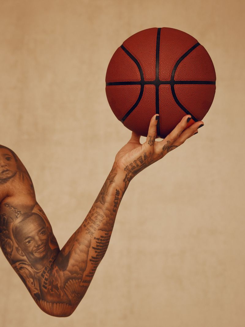 Tattooed arm of a man holding a basketball in his hand against a neutral background, studio lighting, and a close-up view.