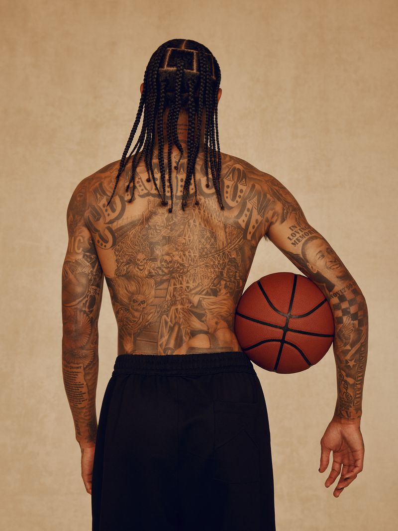 Athletic man's back with intricate tattoos, braided hair, and a basketball in a studio setting, showcasing fitness and style.