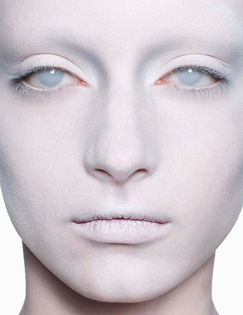 Close-up of a person's face with pale white skin and light eyes, featuring makeup and a striking, monochromatic color scheme in a studio setting.