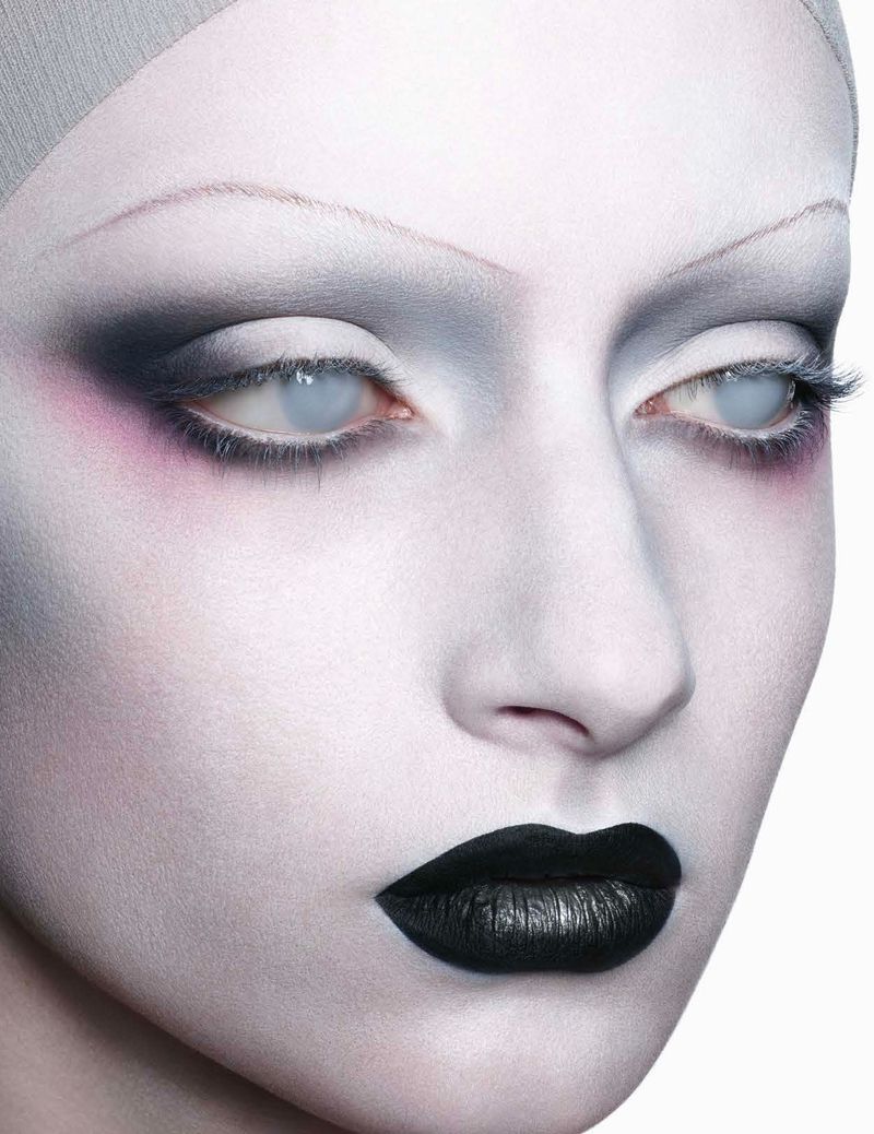 Close-up of a person with dramatic white and black makeup, including white eyes and black lips, against a bright white backdrop.