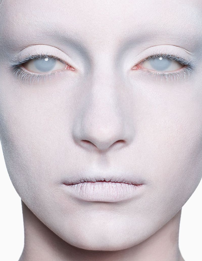 Close-up portrait of a person with face paint, white skin, and light eyes looking directly at the camera in a high key image.