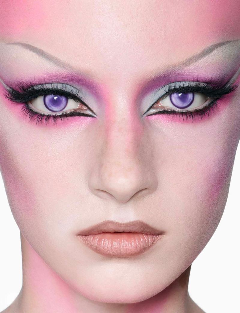 Close-up of a woman's face with pink makeup and purple eyes, enhanced by dramatic black eyeliner and false eyelashes, against a white background.