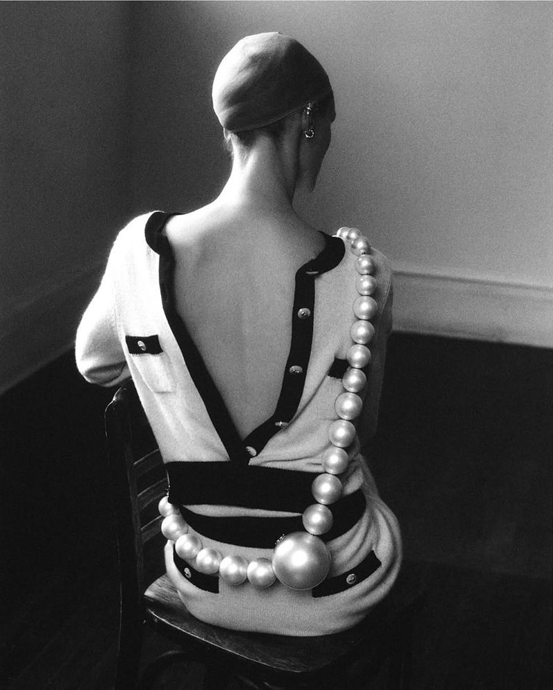 Black and white fashion shot featuring a woman wearing a sweater dress with pearl embellishments and a matching cap, shot from behind.