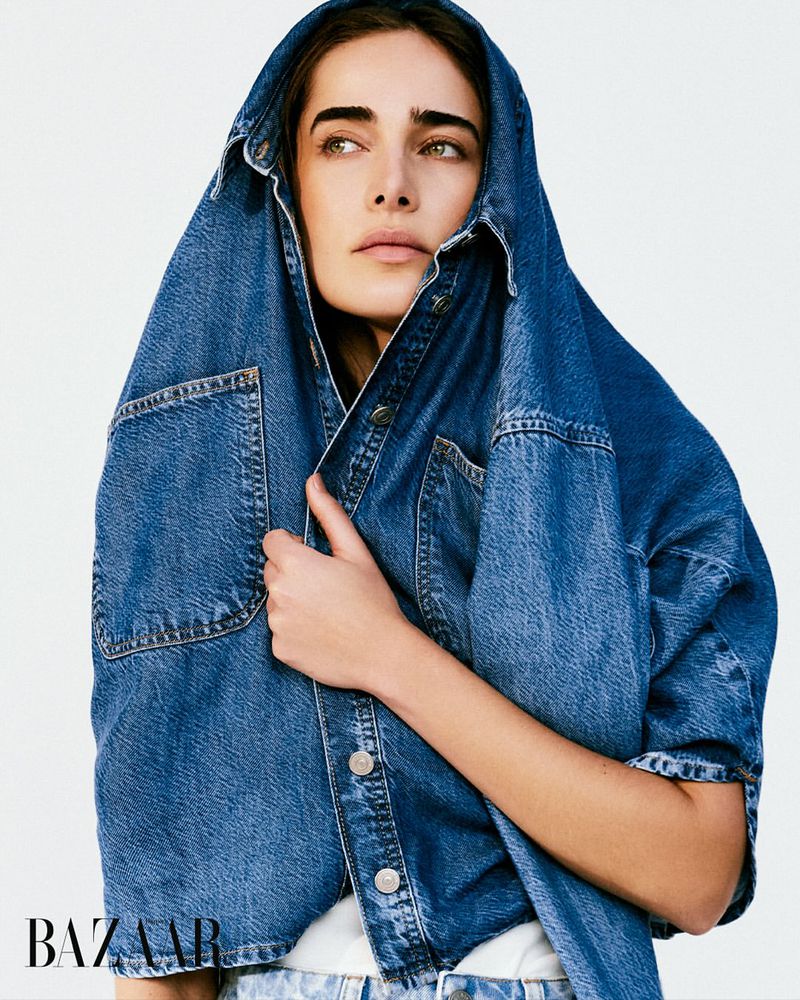 Woman poses indoors wearing a denim shirt over her head against a white background in a fashion style portrait shot.