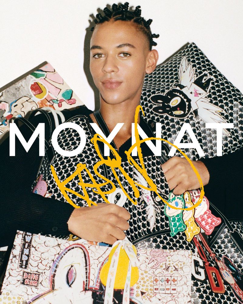 Portrait of a stylish adult male holding designer handbags. The model wears a black top, the MOYNAT logo is shown with custom artwork.