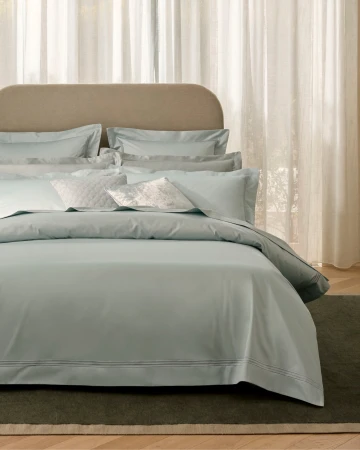 Luxurious bed with light blue bedding, including a duvet cover, pillows, and shams. A neutral headboard complements the cool-toned linen.