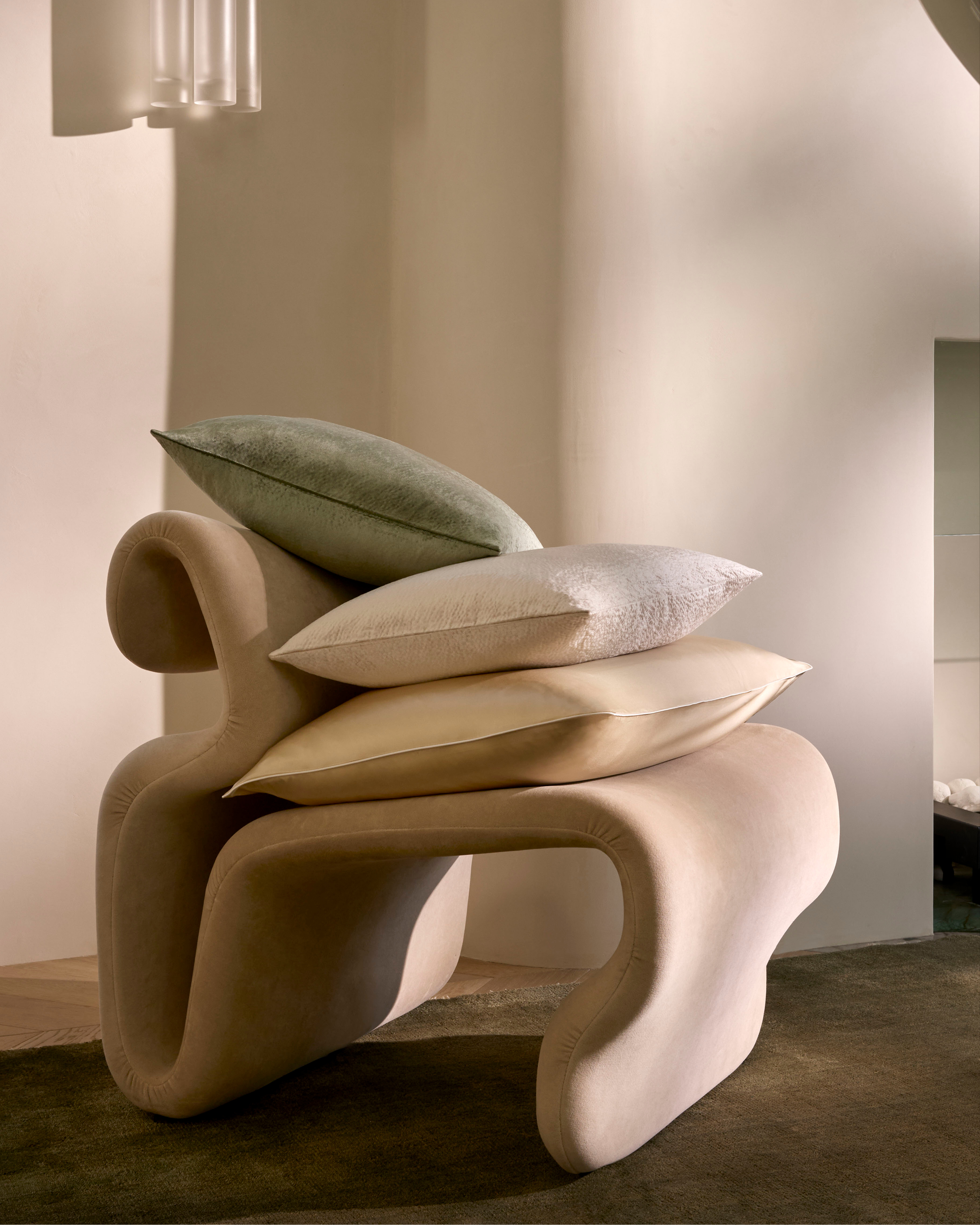 Neutral-toned interior featuring a modern sculptural chair with three soft pillows stacked on top, creating a cozy and inviting scene.