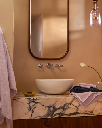 Bathroom interior featuring a white vessel sink, marble countertop, mirror, and a towel, creating a clean and modern aesthetic.