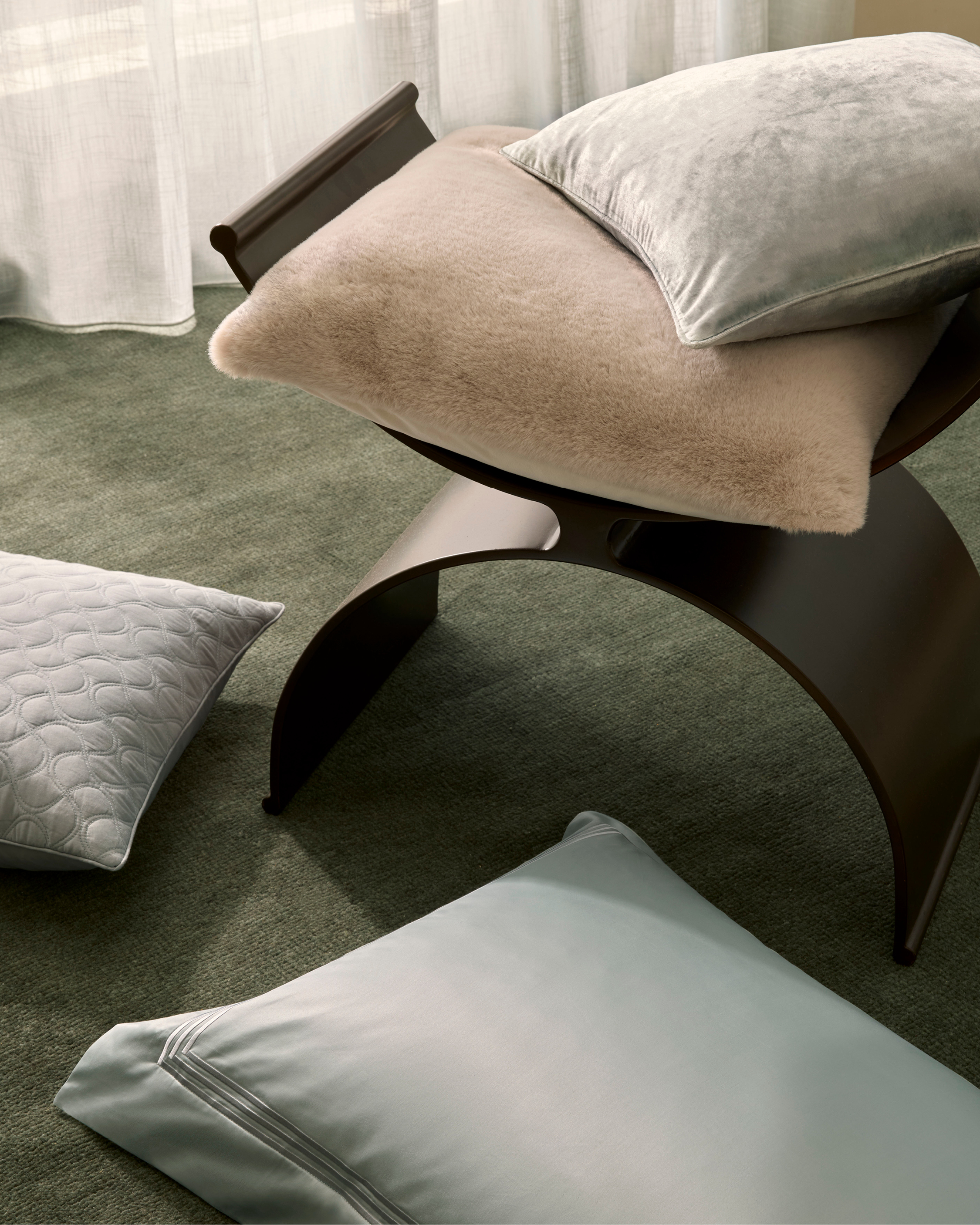 Living room interior with a dark wood bench seat covered with pillows in shades of grey and tan on top of a green carpet.