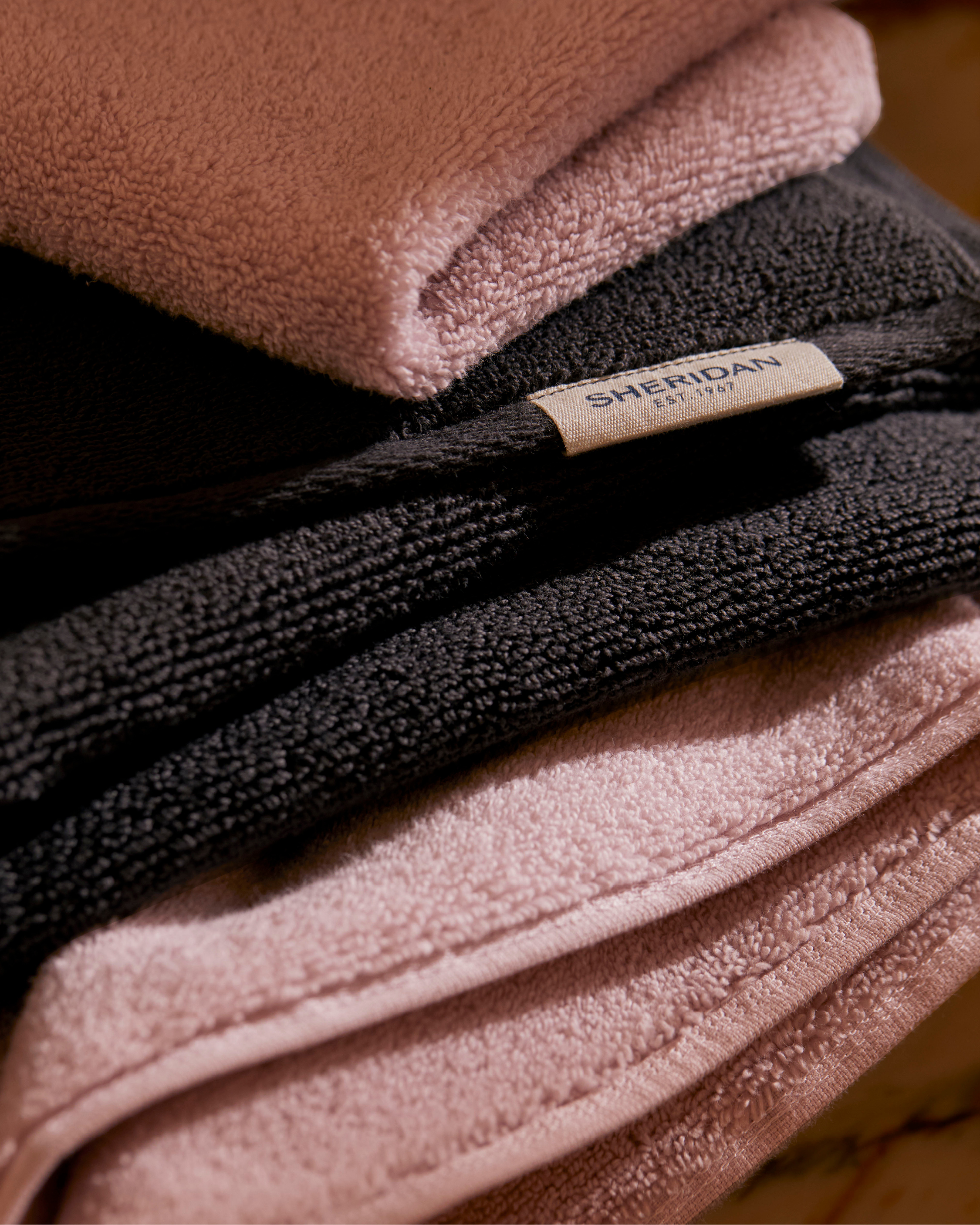 Stack of folded Sheridan towels in pink and gray, showcasing soft texture and brand label, ideal for bath or home decor product.