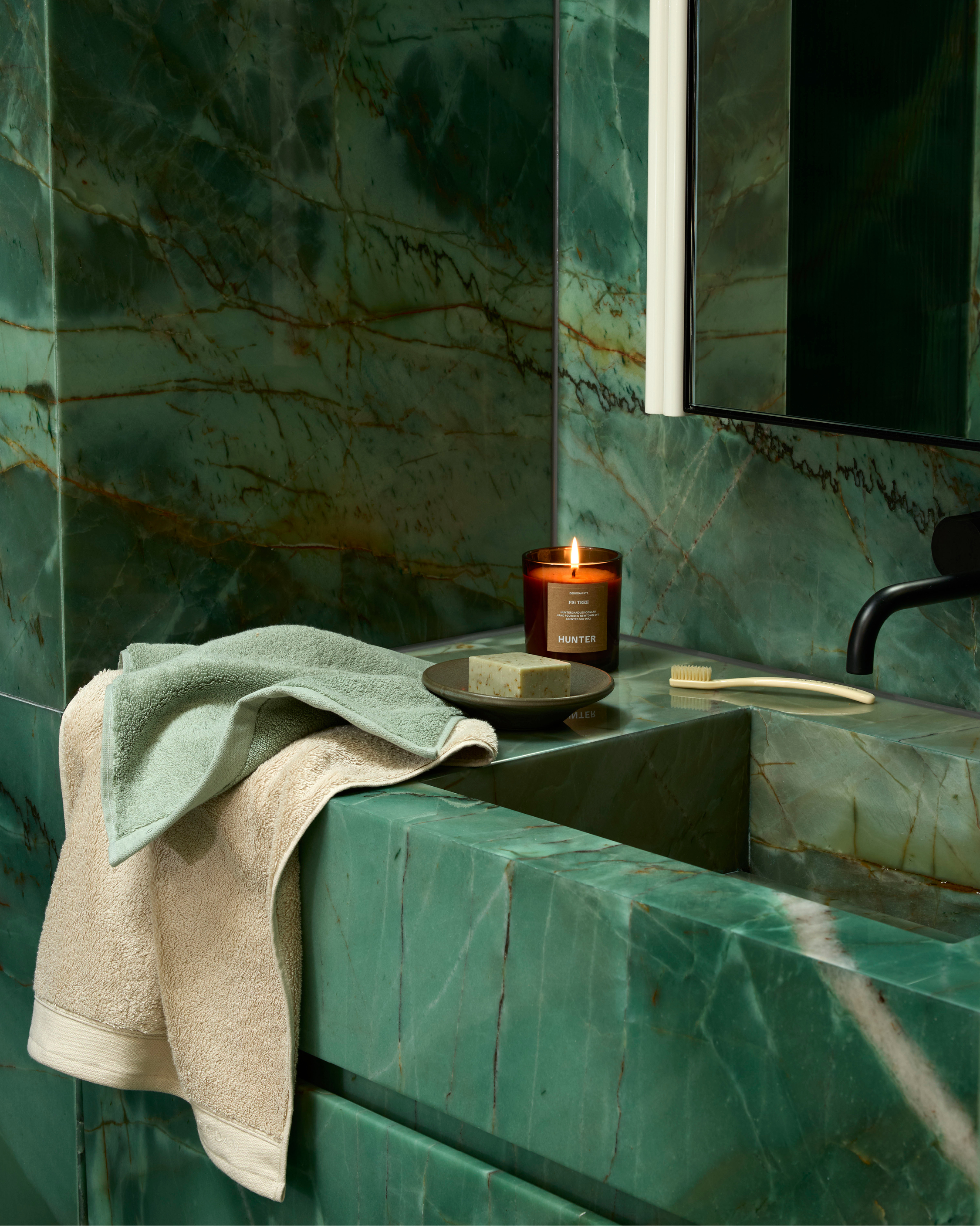 Luxurious bathroom interior featuring green marble walls, a textured towel, soap, toothbrush, and a lit candle for a relaxing ambiance.