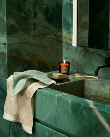 Luxurious bathroom interior featuring green marble walls, a textured towel, soap, toothbrush, and a lit candle for a relaxing ambiance.