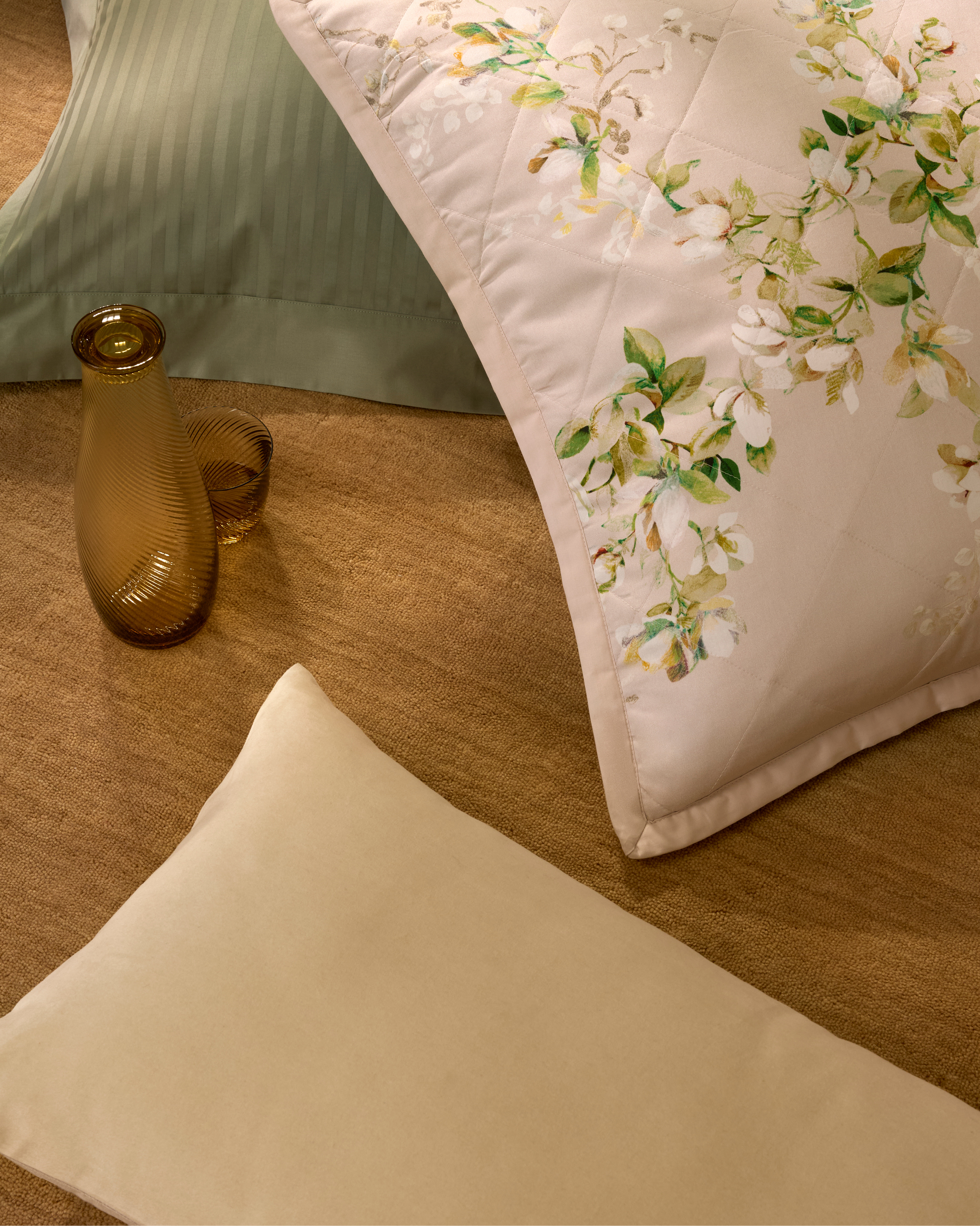 Bedroom decor featuring a floral patterned duvet and pillows, set against a textured brown background and amber glass vase.