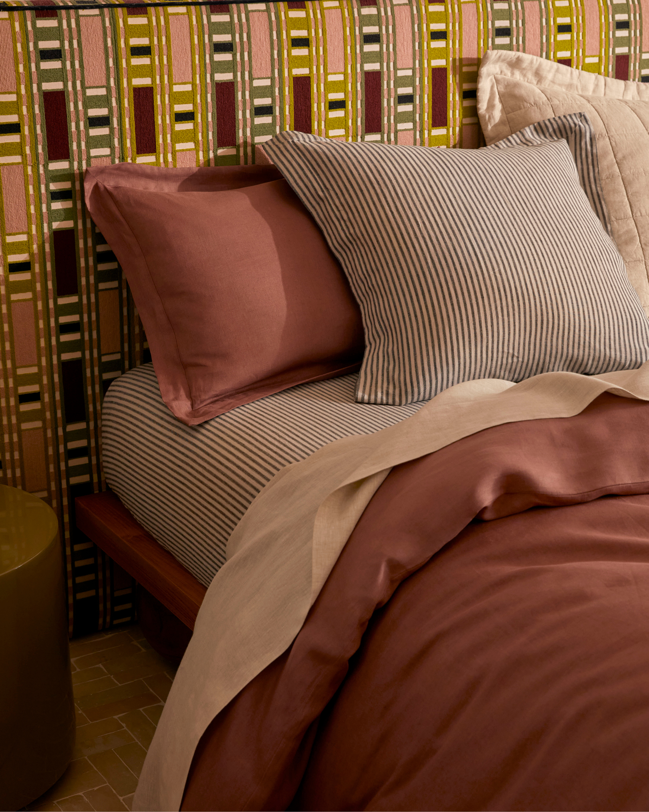 Bedroom interior with a made bed featuring patterned bedding, striped pillows, and a colorful patterned headboard creating a cozy scene.
