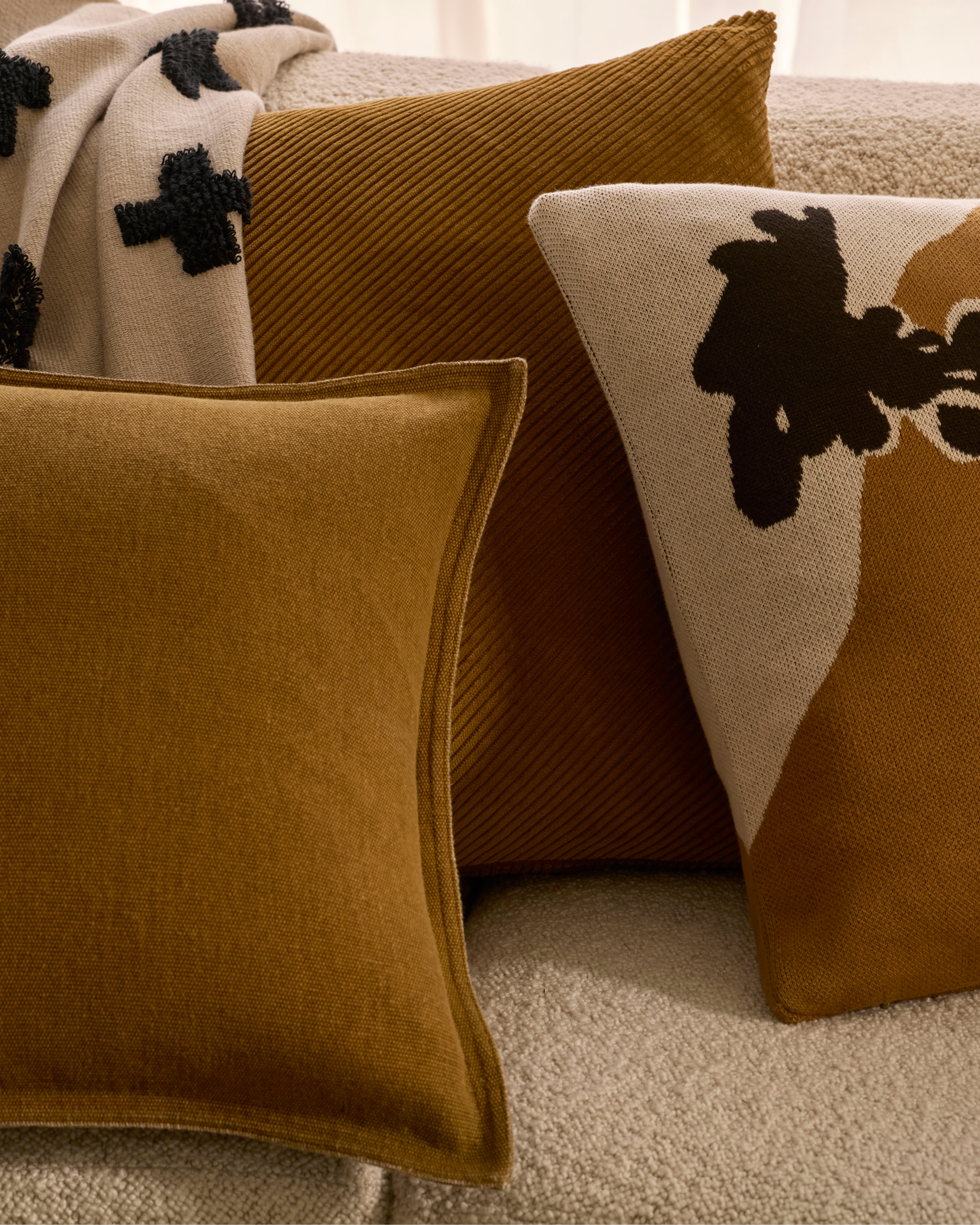 Close-up on a group of throw pillows in neutral tones with different patterns, creating a cozy and textured interior decor arrangement.