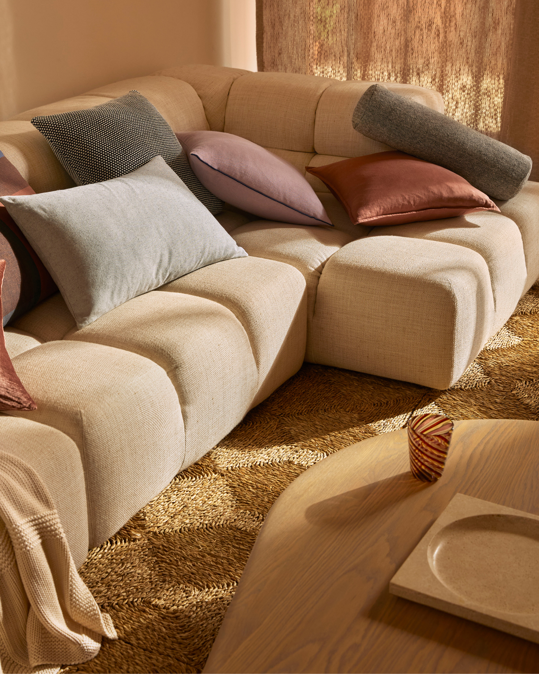 Interior showcasing a modular sofa with cushions, a round wooden coffee table, and a textured rug, creating a cozy, neutral-toned living space.