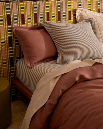 Close-up of a neatly made bed with mauve and striped pillows against a patterned headboard for Sheridan lifestyle shoot