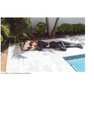 A young adult woman lies on a pillow on a tiled patio next to a pool in a black top and pants outdoors during daytime.
