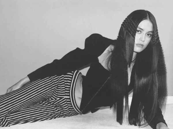 Model Mimi Dey reclining on the floor wearing a structured black top and striped trousers in a black and white editorial shoot.