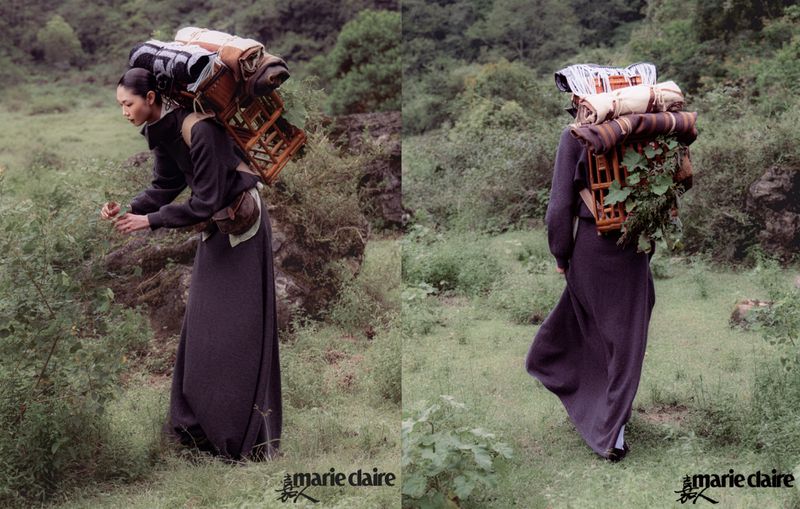 Woman in a long dress carries a basket full of blankets on her back, standing in a grassy field with trees; fashion editorial, lifestyle.