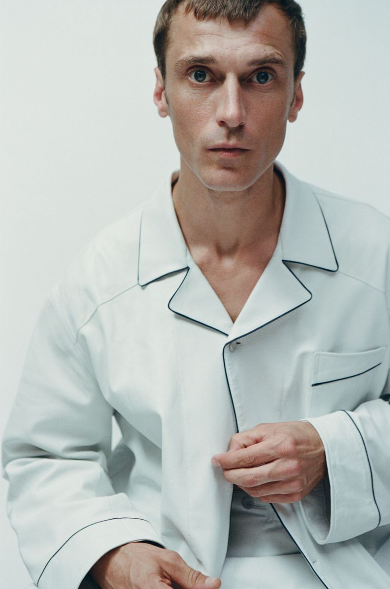 Close-up portrait of an adult male in a white button-down shirt with black trim against a neutral backdrop in a photo studio setting.