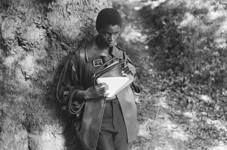 Model Onyinyechi Chijioke leaning against a large tree holding a structured handbag in 10 Magazine