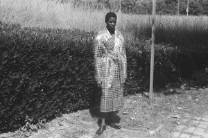 Model standing outdoors wearing a patterned belted coat in front of hedges for 10 Magazine