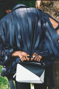 Onyinyechi Chijioke seen from behind wearing a sculptural navy fringe jacket and holding a black and white geometric handbag.