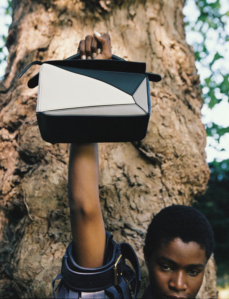 Black and white handbag raised by a black woman in front of a tree with green leaves. Focus on the high fashion purse. 