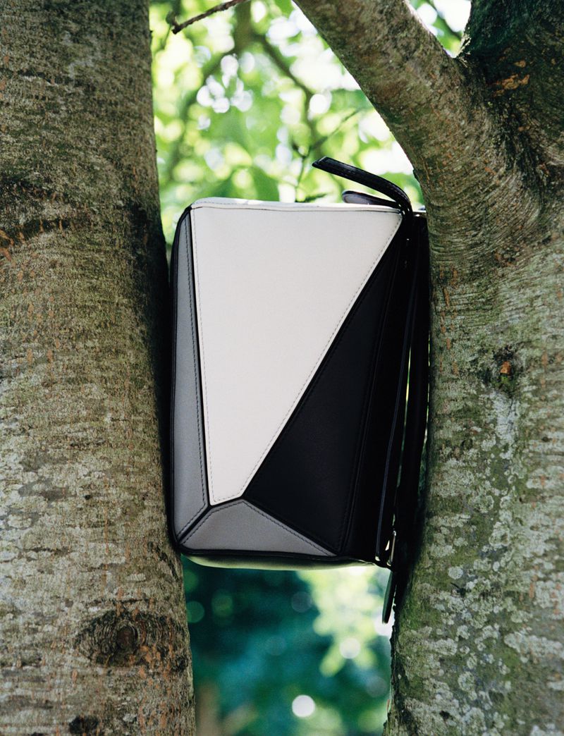 Geometric handbag in black, white, and gray displayed within the branches of a tree, set against a backdrop of lush green foliage.