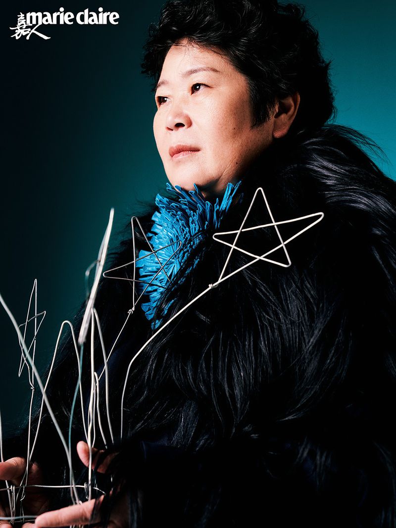 Portrait of an Asian woman with short black hair, wearing a dark coat and a blue top, posing with star-shaped props in a dark studio.