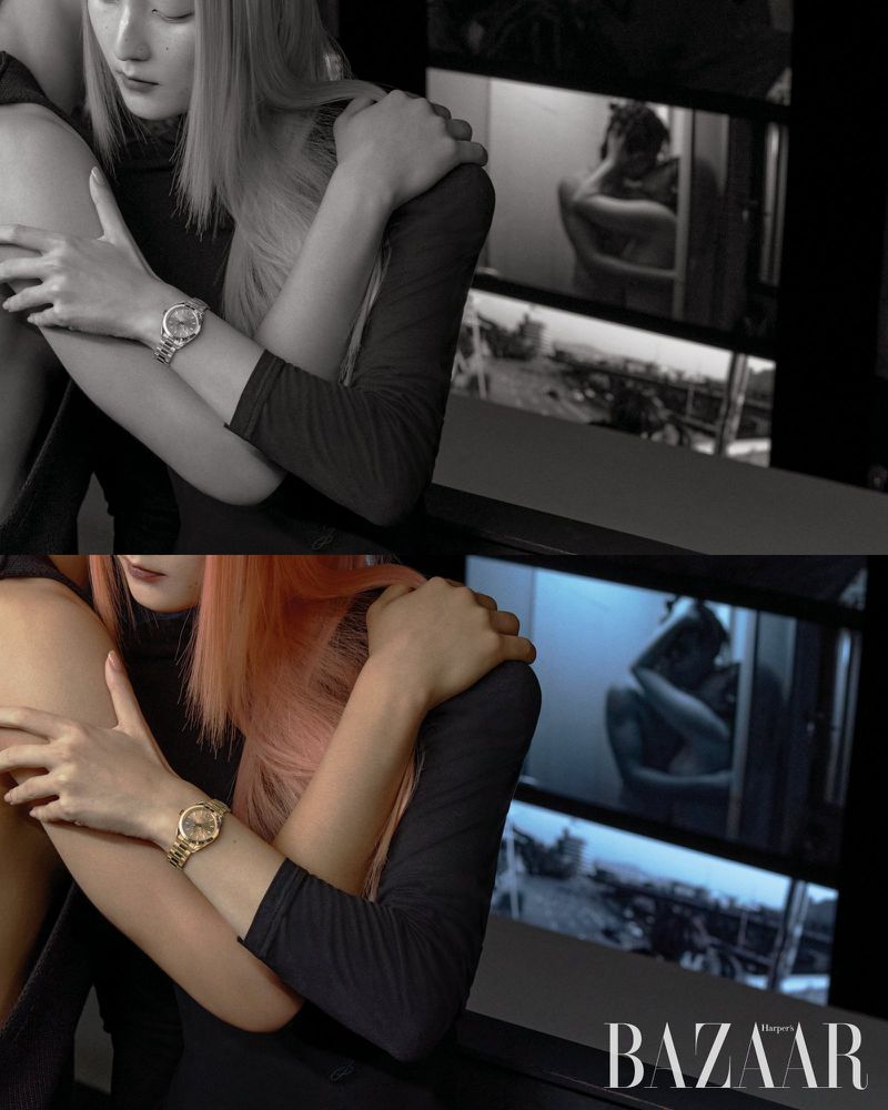 Fashion editorial shot of two women with blonde and pink hair, wearing black outfits, showcasing a gold wristwatch in an indoor setting.