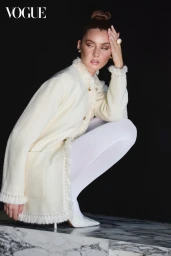 Model in cream tweed jacket and white tights crouching on a marble ledge against a black background for Vogue China Kellery project