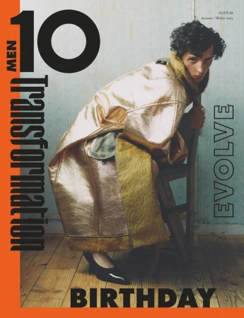 Fashion magazine cover featuring a young adult in a metallic gold coat, seated on a wooden chair in front of a textured backdrop.