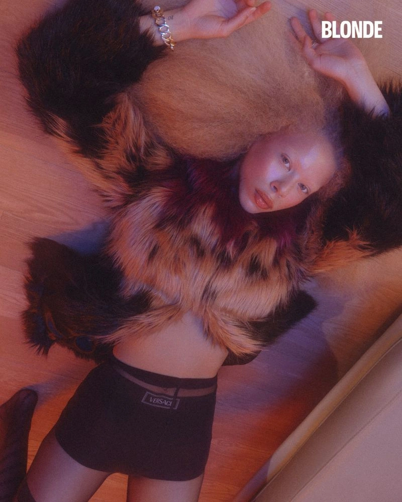 Model lying on wooden floor wearing a furry patterned coat and dark shorts for BLONDE Magazine editorial