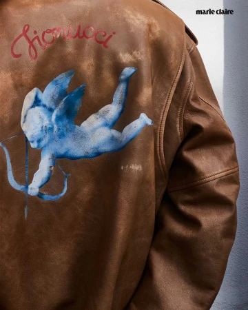 Brown leather jacket with a blue angel design and 'Fiorucci' text, set against a neutral background, Marie Claire logo in upper right.