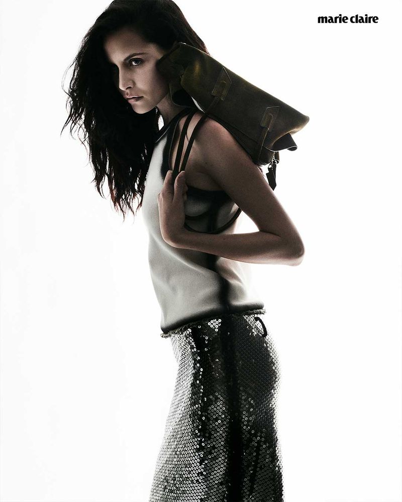 Fashion editorial shot of a slender woman with long dark hair modeling a sleeveless top, sequined skirt, and a bag over her shoulder.