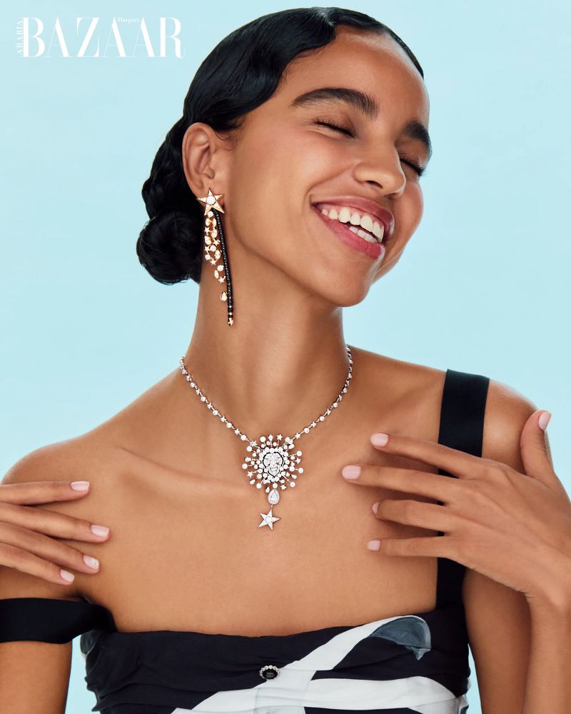 Close-up of a woman with dark hair, wearing a black and white dress and jewelry, including a necklace and star-shaped earrings.