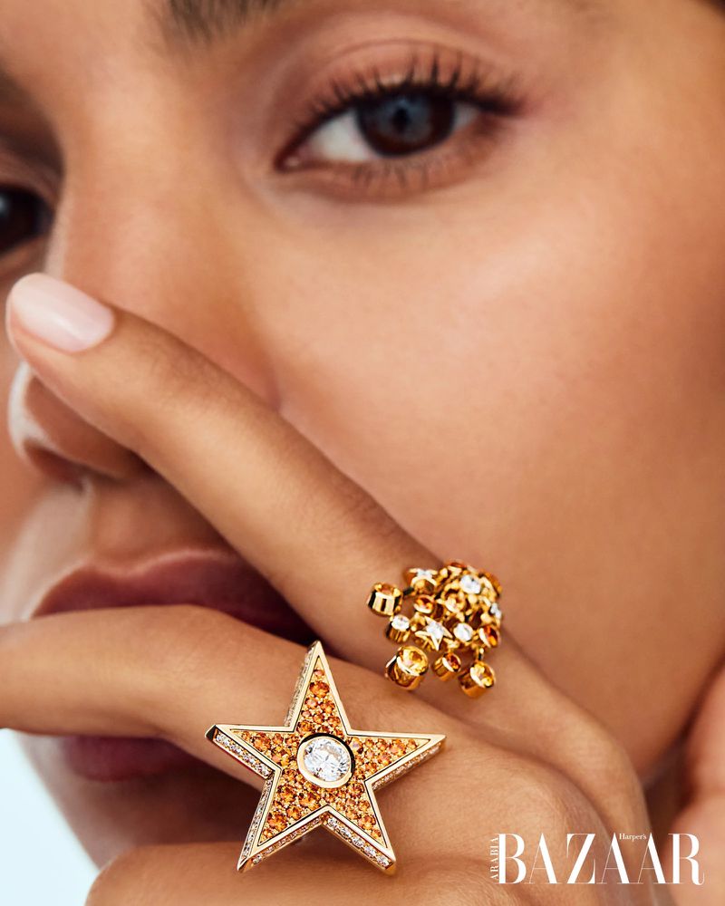 Close-up shot featuring an adult female model wearing two gold rings, one star-shaped, against a soft, neutral-toned background.