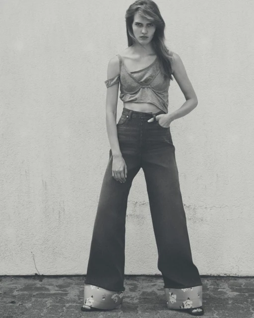 A stylish woman in a crop top and wide-leg jeans poses against a wall in a black-and-white fashion shot with vintage flair and bold design.