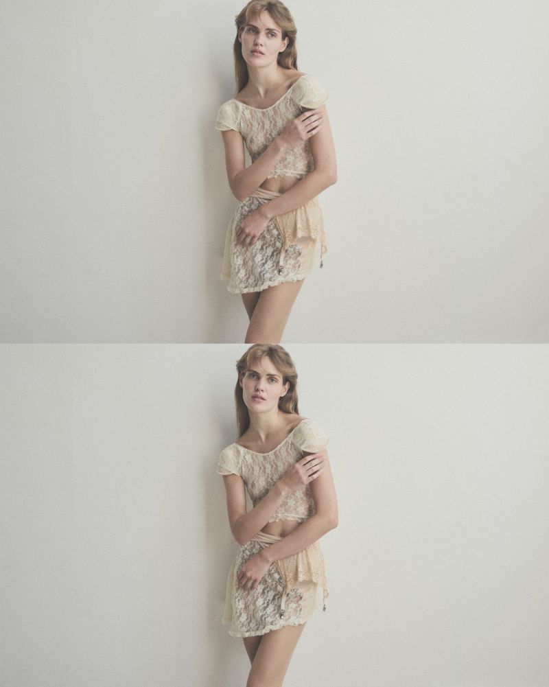 Woman in lace top and skirt posing against a white wall in a fashion studio; soft, diffused lighting enhances the delicate texture.