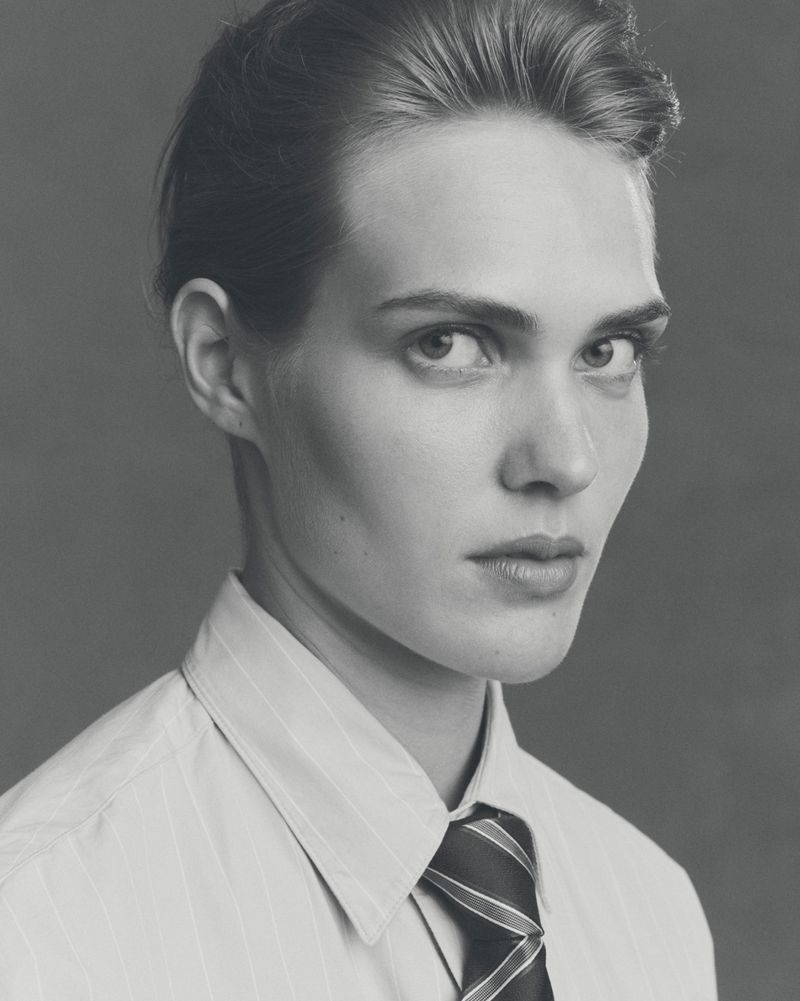 Monochrome portrait of an adult male in a striped shirt and tie, looking at the camera with a neutral expression against a grey backdrop.
