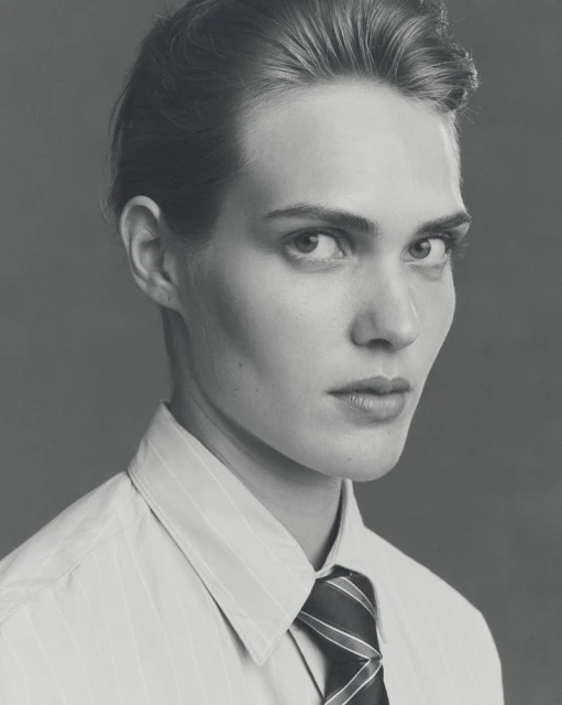 Monochrome portrait of an adult male in a striped shirt and tie, looking at the camera with a neutral expression against a grey backdrop.