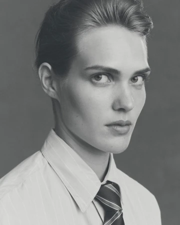 Monochrome portrait of an adult male in a striped shirt and tie, looking at the camera with a neutral expression against a grey backdrop.