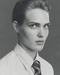 Black and white portrait of a model with slicked-back hair wearing a pinstripe button-up shirt and striped tie.